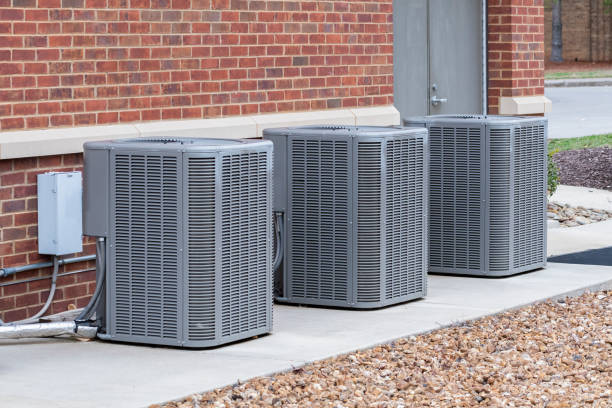 Three outdoor air conditioning condenser units installed outside a residential brick building
